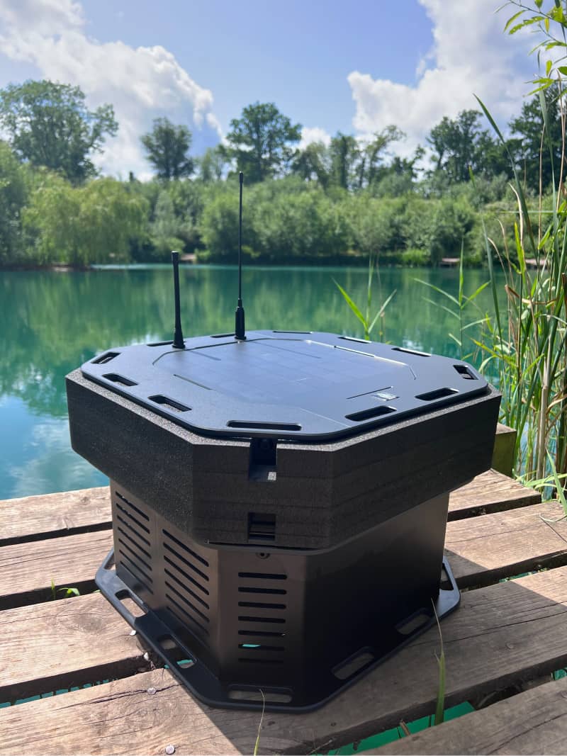 Photo of the WATR Pro unit sitting on a dock next to a lake, showing the solar panel and antenna